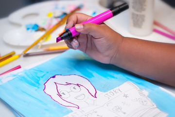 A little kids hand holding a pink art marker and coloring inside the lines of a hand drawn illustration using mixed media.