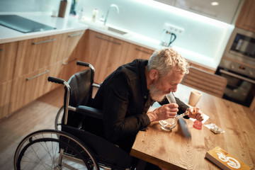 Seeking help. Disabled man in wheelchair lighting cannabis in the bowl of glass water pipe or bong...