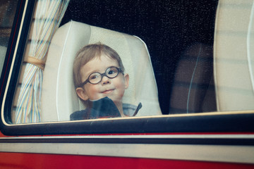 A little boy with round glasses looks through the bus window before leaving (vintage processing, noises, film photo)