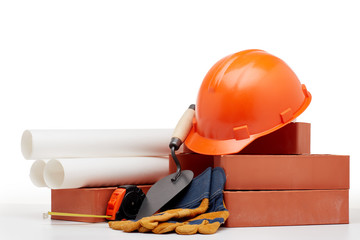 Architectural blueprints, stack of bricks, masonry trowel,  construction hard hat on white background. Construction concept.