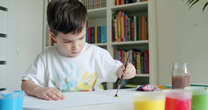 Preschooler boy painting on paper with his left hand. Little boy with paintbrush and colorful paints. Hand-held shot, single shot, medium close up, 4K.