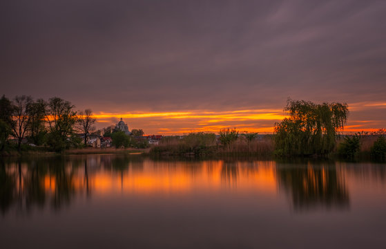 Long exposure sunset view on Ivano-Frankove (Yaniv), Yanivskyi Stav Lake and forest. Roztochia Biosphere Reserve, Lviv district, Ukraine. May 2020
