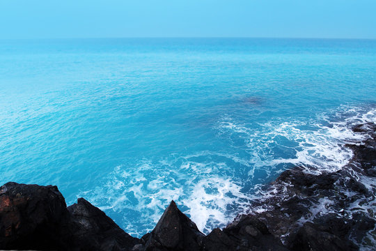Ocean waves on the black volcanic cliffs, stormy day, top view. Storm season, seascape, black rocks