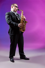 Fototapeta premium Music and Musicians Concepts. Full length Portrait of Mature Expressive Caucasian Saxophonist Against Colorful Background.