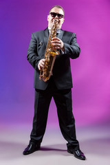 Musicians Concepts. Full Length Portrait of Mature Expressive Caucasian Saxophonist Against Colorful Background.