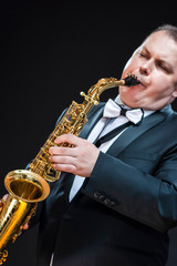 Obraz premium Music Concepts. Portrait of Passionate and Extravagant Caucasian Saxophonist in Dark Suit Posing in Sunglasses Against Black Background.