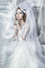 A shining snow queen with a crown in a castle with a veil in the snow. Creative makeup in blue colors