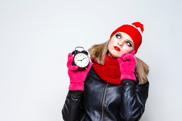 Time Concepts. Portrait of Thoughtful  Caucasian Girl In Warm Hat and Scarf Posing With Mournful Expression. Holding Round Clock On Hand Against White.