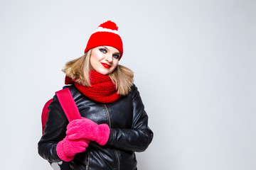 Portrait of Caucasian Blond Girl In Warm Hat and Scarf Posing in Jacket With Backpack Against White.