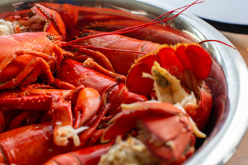 Lobster in a large metal bowl. The whole red shellfish has been steamed a bright red colour. The colourful fresh seafood has delicious lobster meat, shells, claws, tails and long bodies in a dish. 