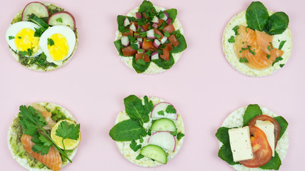 Beautiful six rice cakes sandwiches with different healthcare ingredients on pink background.Tasty rice cakes with tomatoes, salmon, mint and others fit vegetables. Healthcare food concept
