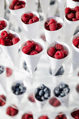 Ripe beautiful red raspberries and blueberry in white glasses. White packaging. Ripe raspberry berries and blueberry in summer.