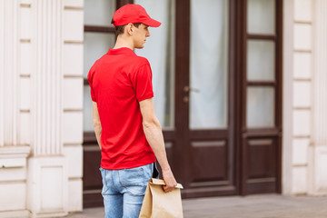 A uniformed courier holds a paper bag of food in the open air