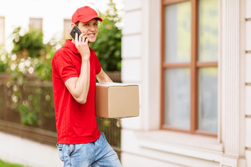 courier with a cardboard box, talking on a mobile phone. Home delivery