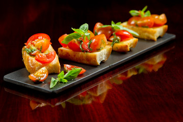 Italian tomato and basil bruschetta, classic antipasto, on baguette bread mini toasted slices. Regional mediterranean cuisine, pomodoro appetizer recipe on dark wooden background. Vegetarian food.