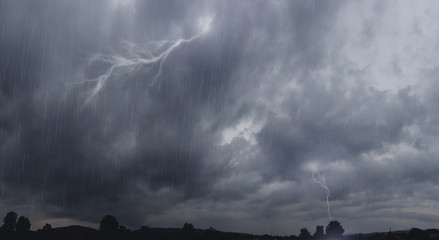Dark stormy clouds on the sky, with striking lightning and heavy rain. Lightning bolts strike from...