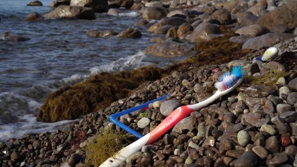 Old used discarded toothbrush in a seashore. Garbage in nature, environment. Plastic that are being...
