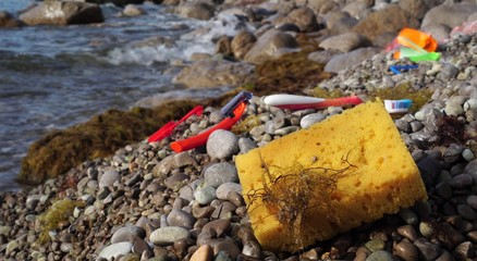 Old used discarded sponge for dishes, toothbrush, disposable razor in a seashore. Plastic waste in...
