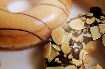 Selective focus of donuts, glazed with melted chocolate and decorated with almond and nuts, lie on a platter.