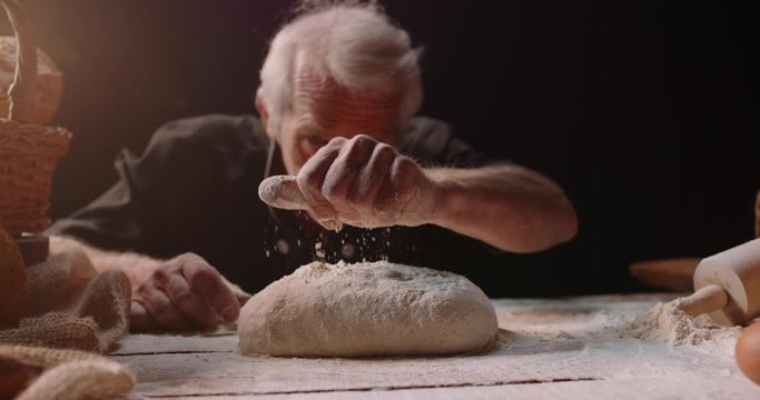 Professional mature caucasian baker putting flour on loaf of bread dough with passion, retired pensioneer enjoying his new hobby, isolated on black background 4k footage