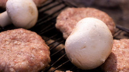 Beef BBQ Cooking of burger meat and mushroom. Iron barbeque grill pan with fire and food. Hamburgers outdoors barbecuing on coals. Closeup beef for burgers on cast iron grill. Juicy fat food grilled.