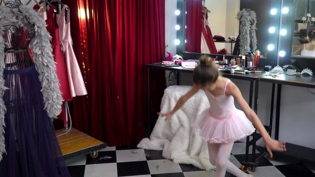 Young beautiful little ballerina girl dancer in pink ballet dress tutu do dance practice in dressing room. Smiling cute child girl in dance costume enjoy and having fun with dancing in make up room.