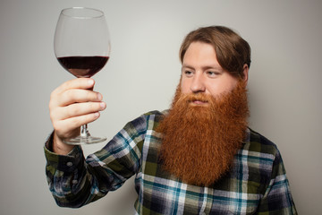 A red-bearded man drinking wine from a large glass. A vine tasting at home. Sommelier for yourself at home. A man with a big beautiful beard.