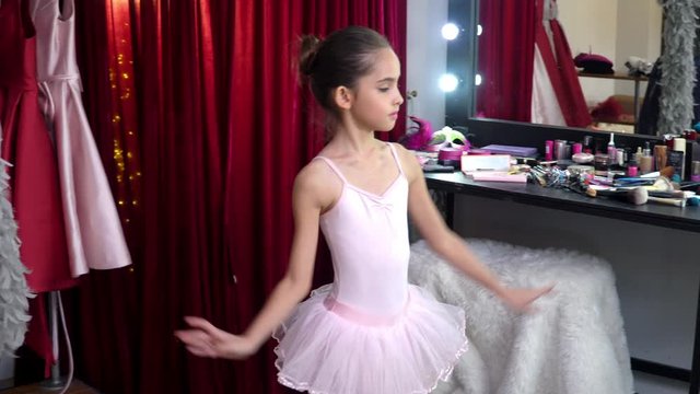 Young beautiful little ballerina girl dancer in pink ballet dress tutu do dance practice in dressing room. Smiling cute child girl in dance costume enjoy and having fun with dancing in make up room.