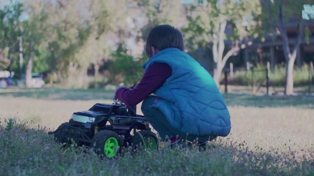 Footage of caucasian boy, playing in a field with remote controlled monster truck toy, back view SLOW MOTION