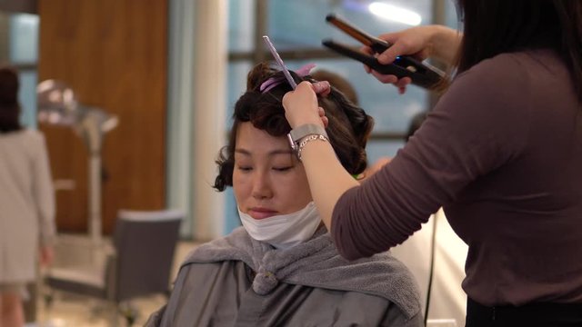 Young Korean woman sits with face mask below her mouth in hair salon, static close up 
