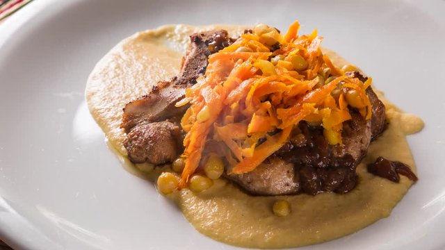 pork chop with barbecue sauce and corn musseline with carrot. Front view with smoke.