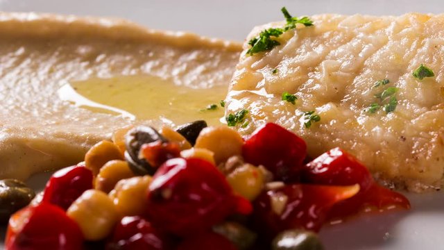 Fish dish - fried fish fillet with chickpeas sauce and vegetables. Front view with smoke.