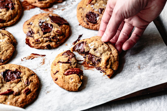 Closeup view of a hand breaking a chocolate chip cookie in half.