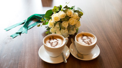 Two mugs with cappuccino on which a heart is drawn with a wedding bouquet of flowers.