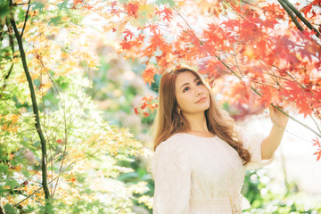 Beautiful asian woman with autumn leaves, flower and fall yellow leaves background at Hagley park, Christchruch, New Zealand.