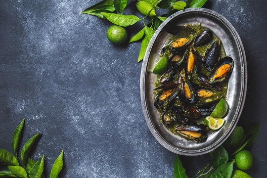 Mussels in green herb and white wine sauce with lemon on dark background.
