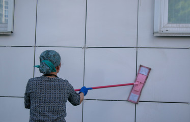A woman washes a ventilated building facade using a mop. View from back. Close-up. Concept of...