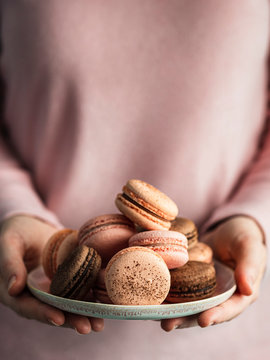 Macarons heap on plate in female hands, vertical