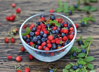 berries of wild strawberries and forest blueberries on a background of nature on an old rustic board. Country style. Soft focus. Space for text