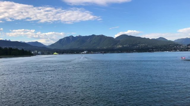 Lake series seaplanes lining up and taking off toward mountains pillowy clouds in blue skies and mountains behind
