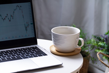Economic crisis. Trader is sitting in home at table, working on laptop with graphics diagrams on white monitor. Cropped computer and drink coffee. Analysis Business, Statistics Concept