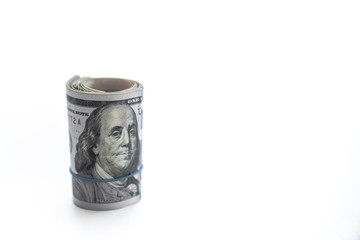 A wad of money is rolled up with a Benjamin or United States hundred dollar bill on the top standing on edge with a blue rubber band isolated on a white background with copy space.