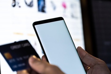 Mock up mobile phone and credit card in hand with monitor background. Concept for mobile application technology and online e-commerce.