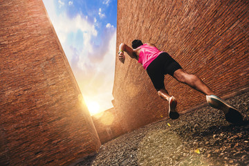 Fit young man at start running. Runner start a race on a rock track with tall red brick wall as...