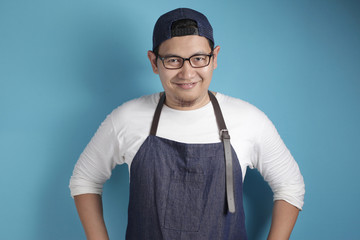 Portrait of happy smiling Asian chef or waiter, good restaurant business concept, against blue background