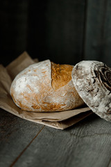 Healthy rye whole grain round bread on brown craft paper on black wooden table. Home baked