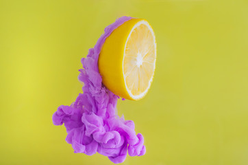 Slice lemon with partial focus of dissolving violet poster color in water on yellow background for...