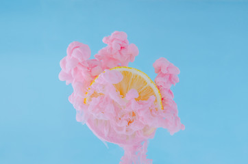 Slice lemon with partial focus of dissolving pink poster color in water on blue background for...