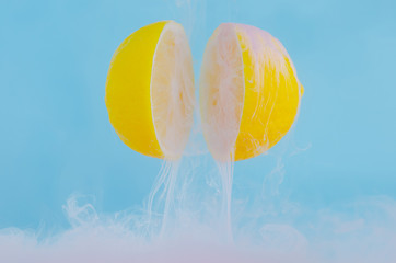 Blurred focus of dissolving pink poster color in water drop between two slice lemons on blue...