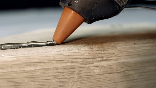 The glue gun squeezes the transparent hot glue onto the wooden part to join the second part into a single structure. Closeup